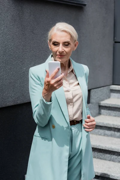 Elderly manager in formal wear using smartphone outdoors — Stock Photo
