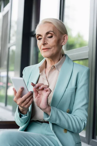 Elderly businesswoman using blurred smartphone outdoors — Stock Photo