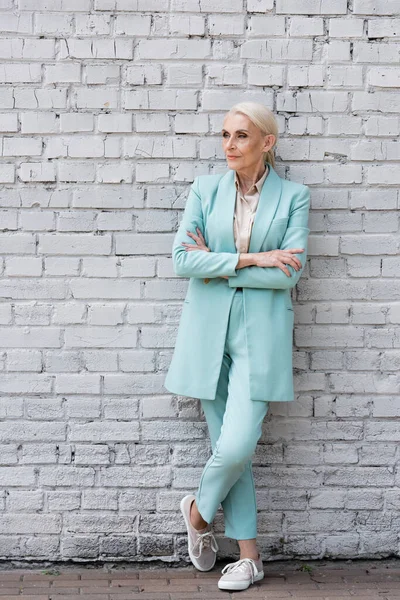 Femme d'affaires âgée debout avec les bras croisés près du mur de briques — Photo de stock