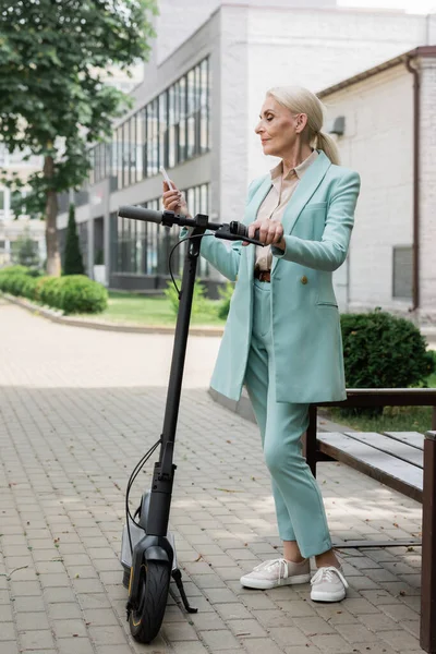 Message femme d'affaires âgée sur téléphone mobile près de scooter coup de pied électrique — Photo de stock