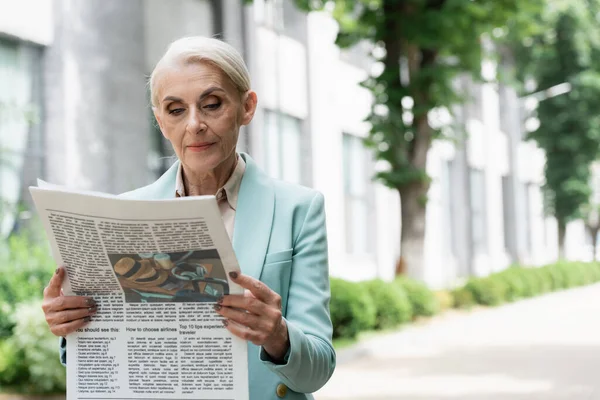 Mujer de negocios senior leyendo el periódico al aire libre - foto de stock