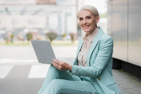 Donna d'affari sorridente seduta sul confine e utilizzando il computer portatile — Foto stock