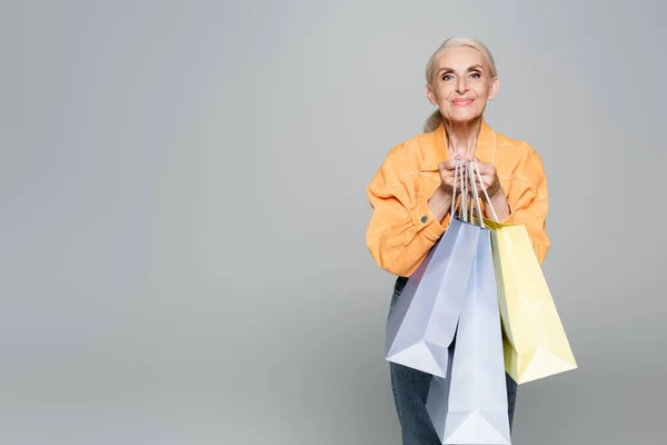 Mujer mayor en chaqueta de moda sosteniendo bolsas de compras aisladas en gris - foto de stock