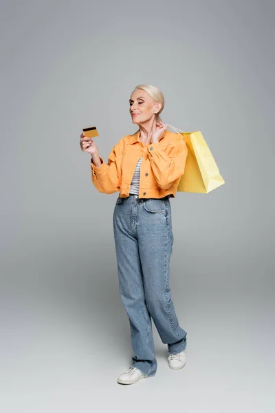 Mulher sênior com sacos de compras olhando para o cartão de crédito em cinza — Fotografia de Stock