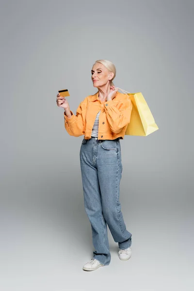 Senior woman with shopping bags looking at credit card on grey — Stock Photo