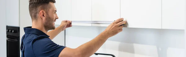 Positive workman measuring cabinets of modern kitchen furniture, banner — Stock Photo