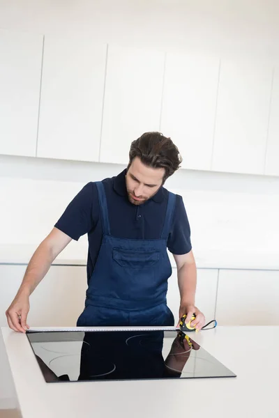 Junger Handwerker misst Elektroherd in moderner Küche — Stockfoto