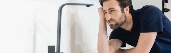 Young plumber looking at faucet in kitchen, banner — Stock Photo