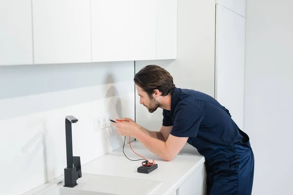 Eletricista verificando tomadas de energia com testador elétrico na cozinha — Fotografia de Stock