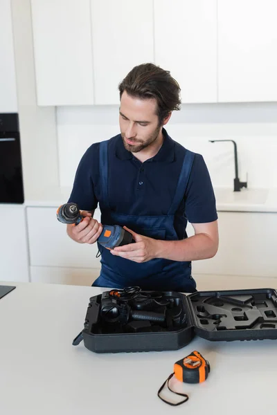 Réparateur tenant perceuse électrique près de cas dans la cuisine — Photo de stock