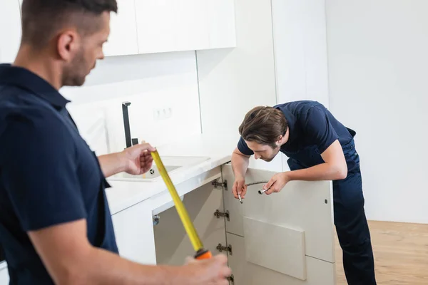 Blurred worker holding measuring tape near plumber with metal hose — Stock Photo