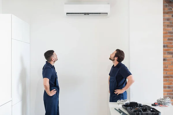 Reparadores olhando para o ar condicionado na parede branca na cozinha — Fotografia de Stock