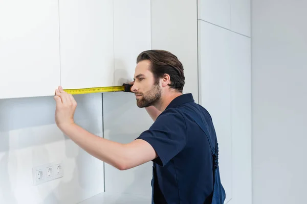 Bricoleur mesurant les meubles blancs dans la cuisine moderne — Photo de stock