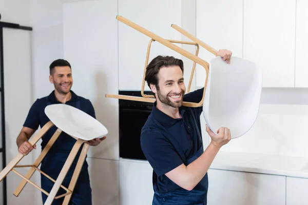 Smiling movers carrying white stools in kitchen — Stock Photo