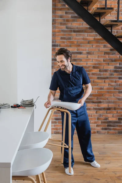 Smiling worker holding stool near wires on white kitchen table — Stock Photo