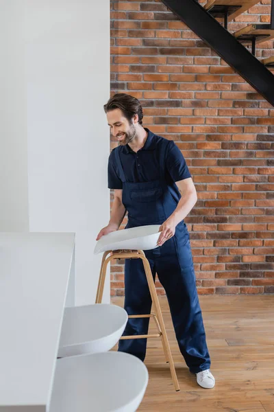 Uomo sorridente che tiene lo sgabello vicino al tavolo bianco in cucina — Foto stock