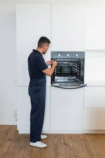 Repairman in overalls fixing electric built-in oven in kitchen — Stock Photo