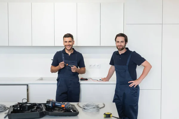 Sorrindo faz-tudo olhando para a câmera perto de ferramentas na mesa da cozinha — Fotografia de Stock