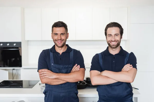 Heureux bricoleurs en uniforme debout avec les bras croisés dans la cuisine — Photo de stock