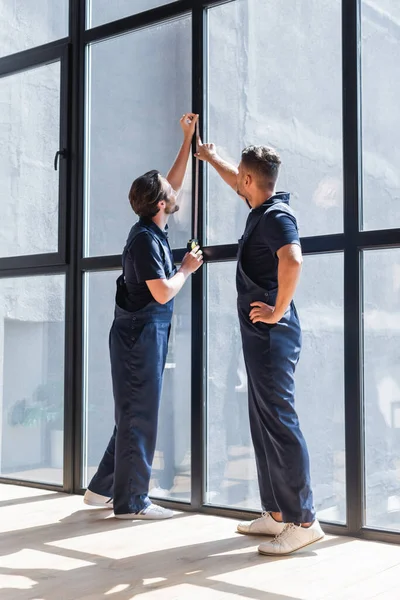 Contremaîtres en salopette mesurant de grandes fenêtres dans un appartement moderne — Photo de stock