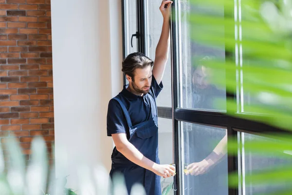 Ouvrier mesurant de grandes fenêtres au premier plan flou — Photo de stock