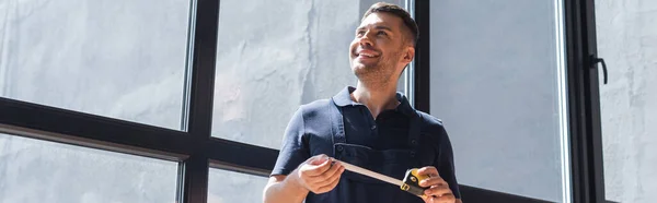 Усміхнений майстер тримає вимірювальну стрічку, стоячи біля вікон, банер — стокове фото