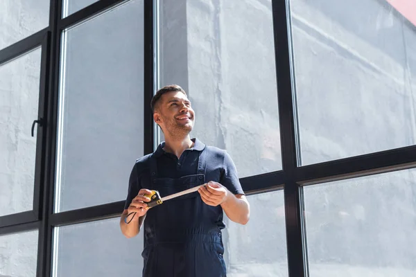 Trabajador feliz de pie cerca de grandes ventanas con cinta métrica - foto de stock