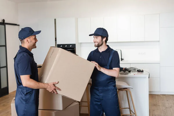 Arbeiter lächeln einander an, während sie Kartons in der Küche halten — Stockfoto