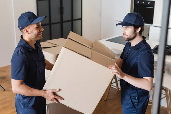 Lächelnder Umzugshelfer hält Karton mit Kollege in Küche — Stockfoto