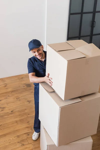 Trabajador positivo apilando grandes cajas de cartón en el apartamento - foto de stock