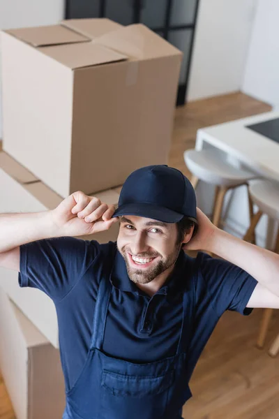 High angle view of cheerful mover adjusting cap while looking at camera — Stock Photo