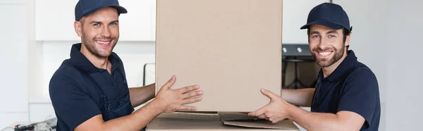 Fröhliche Handwerker lächeln in die Kamera, während sie Pappschachtel, Banner in der Hand halten — Stockfoto