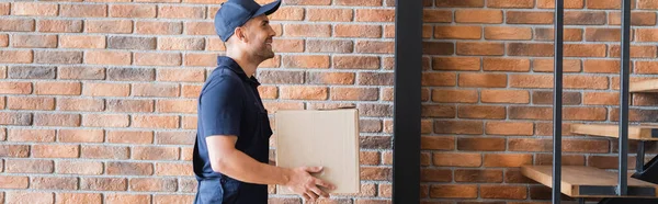 Seitenansicht des lächelnden Mover Tragepakets in der Nähe der Ziegelwand, Banner — Stockfoto