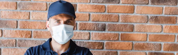 Workman in cap and medical mask looking at camera near brick wall, banner — Stock Photo