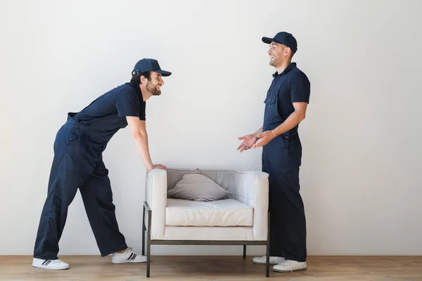 Side view of cheerful mover pointing at armchair near colleague — Stock Photo