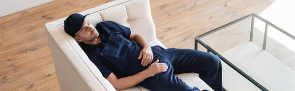 Hochwinkelaufnahme eines Mannes in Overalls, der auf weißer Couch ruht, Banner — Stockfoto