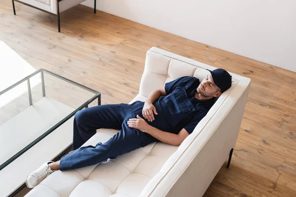 Hochwinkelblick auf müde Mover, die es sich auf weißem Sofa in der Nähe von Glastisch gemütlich machen — Stockfoto
