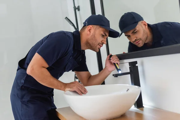 Plumber checking sink with flashlight in modern bathroom — Stock Photo