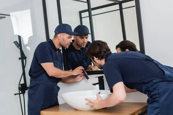 Plumbers checking sink in bathroom with flashlight — Stock Photo