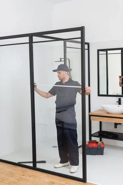 Repairmen in uniform measuring modern shower cabin in bathroom — Stock Photo