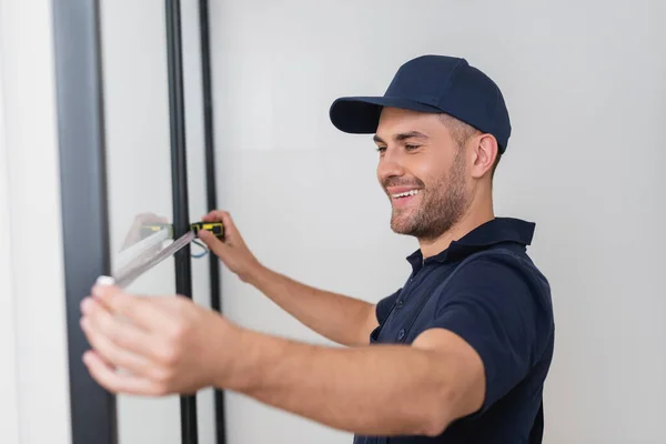 Trabalhador sorridente na tampa usando fita métrica no banheiro — Fotografia de Stock