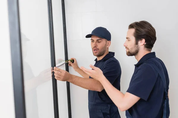 Arbeiter zeigt mit der Hand in die Nähe des Kollegen und misst Duschkabine im Badezimmer — Stockfoto