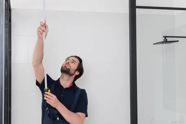 Young handyman measuring shower cabin with measuring tape — Stock Photo