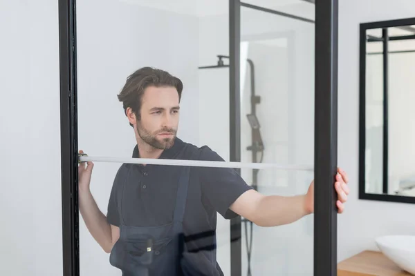 Young foreman measuring shower cabin in modern bathroom — Stock Photo