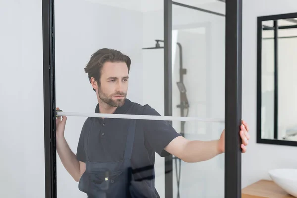 Joven capataz medir cabina de ducha en baño moderno - foto de stock