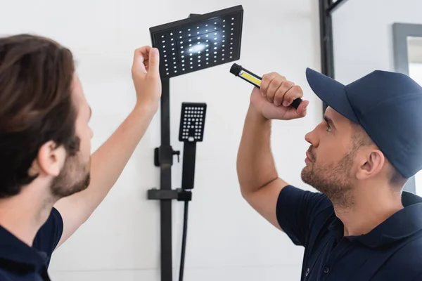 Encanadores com lanterna olhando para a cabeça do chuveiro no banheiro — Fotografia de Stock