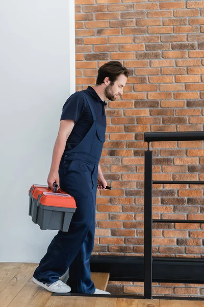 Junger Arbeiter mit Werkzeugkiste und Taschenlampe läuft in Wohnung die Treppe hinunter — Stockfoto