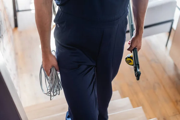Vista parcial del trabajador con cable, llave ajustable y cinta métrica caminando arriba - foto de stock