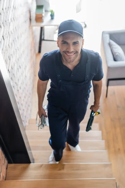 Vue grand angle de l'ouvrier souriant marchant à l'étage avec des fils et des outils — Photo de stock