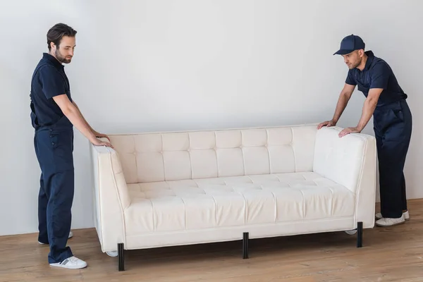 Movers in uniform standing near white couch in living room — Stock Photo